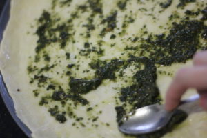 Spreading pesto on the pizza crust for Green Pesto Pizza @ bestwithchocolate.com
