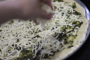 Sprinkling cheese on the pizza crust for Green Pesto Pizza @ bestwithchocolate.com