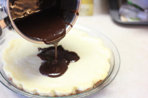 Pouring chocolate ganache over S'mores Cheesecake @ bestwithchocolate.com