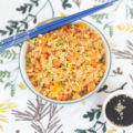 Single bowl of vegetable fried rice with blue chopsticks and soy sauce with sesame seeds