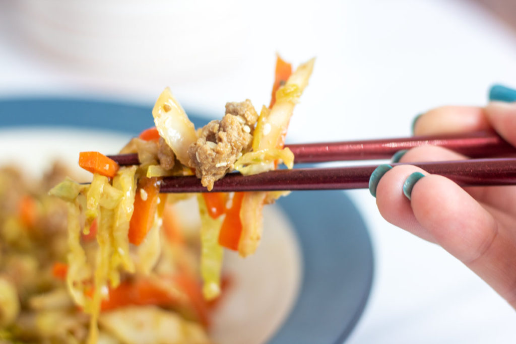 Closeup of chopsticks holding eggroll in a bowl
