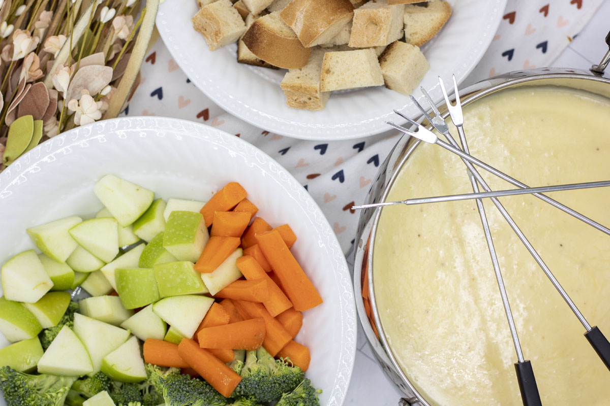 Spread of alpine cheese fondue, carrots, apples, broccoli, and bread cubes
