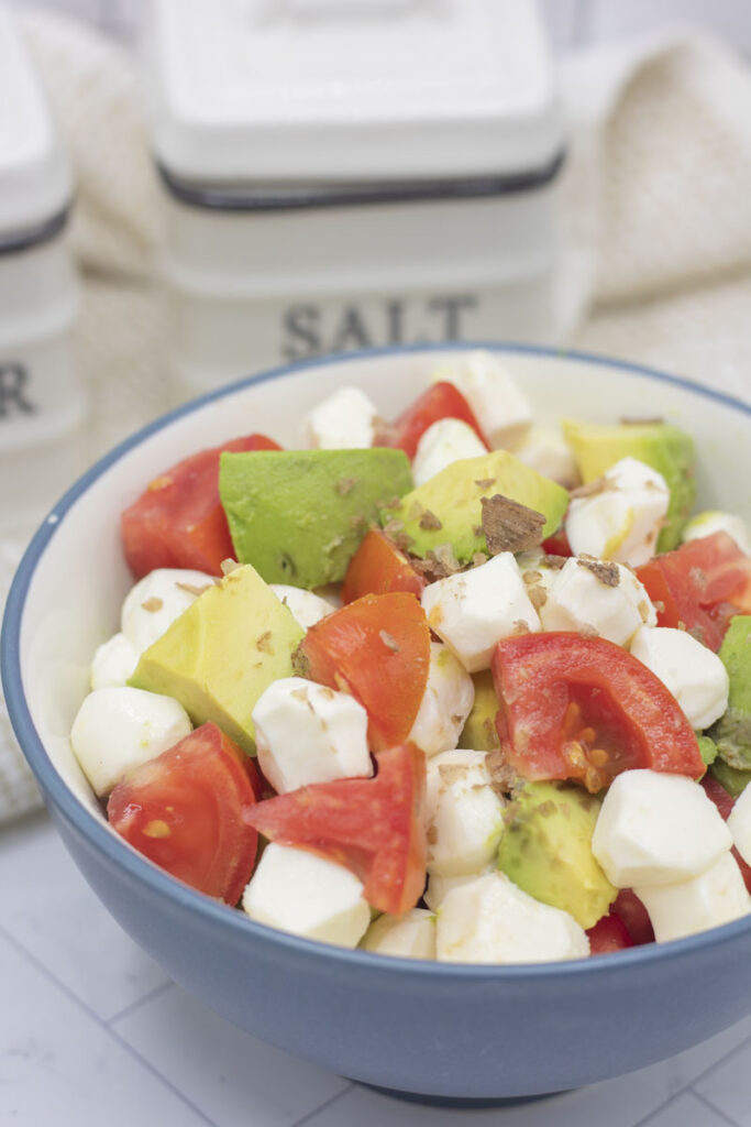 Bowl of caprese salad with chunks of tomato and avocado, and pearls of mozzarella cheese