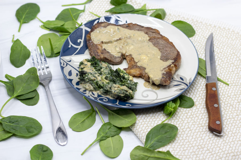 Gorgonzola creamed spinach with a steak on a bed of spinach leaves