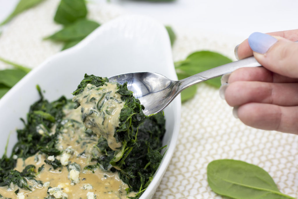 hand scooping a spoonful of blue cheese creamed spinach from a bowl