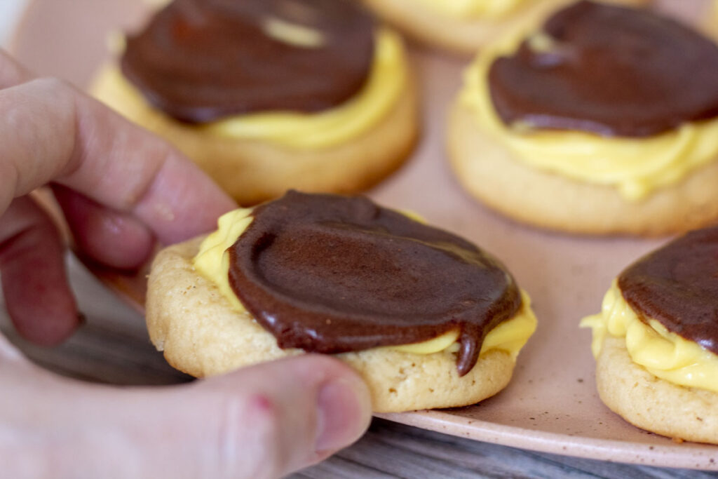 Hand picking up a boston cream cookie from a plate