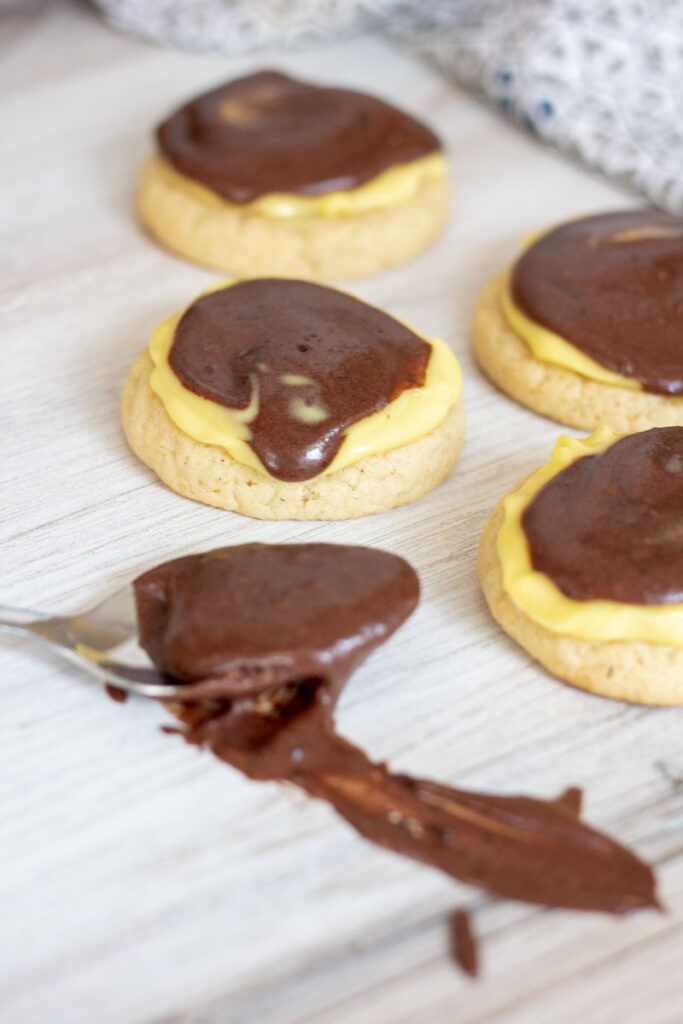 Boston cream cookies scattered around with a schmear of chocolate icing on a spoon