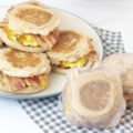 Individually wrapped meal prep breakfast sandwiches next to a plate of unwrapped breakfast sandwiches