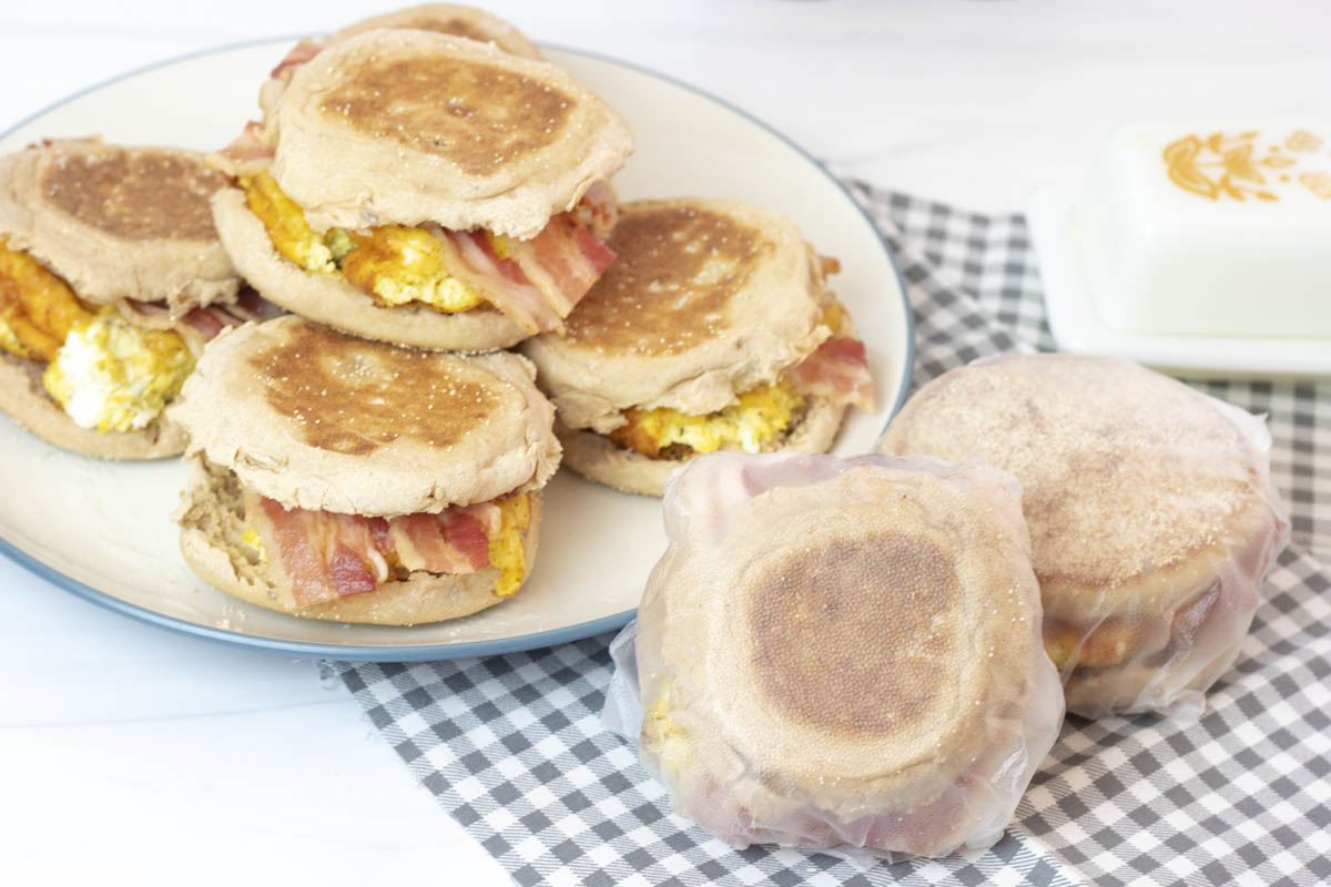 Individually wrapped meal prep breakfast sandwiches next to a plate of unwrapped breakfast sandwiches
