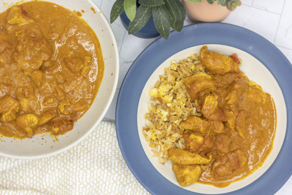 Butter chicken curry and rice in a bowl next to a serving bowl