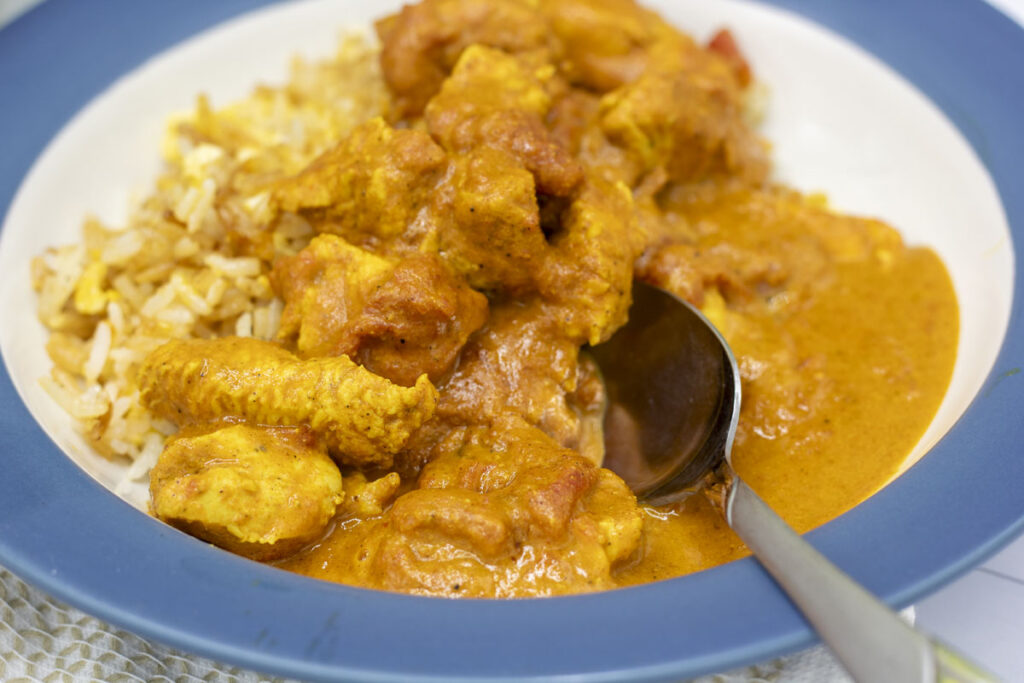 Spoon tucked into a bowl of butter chicken curry and rice