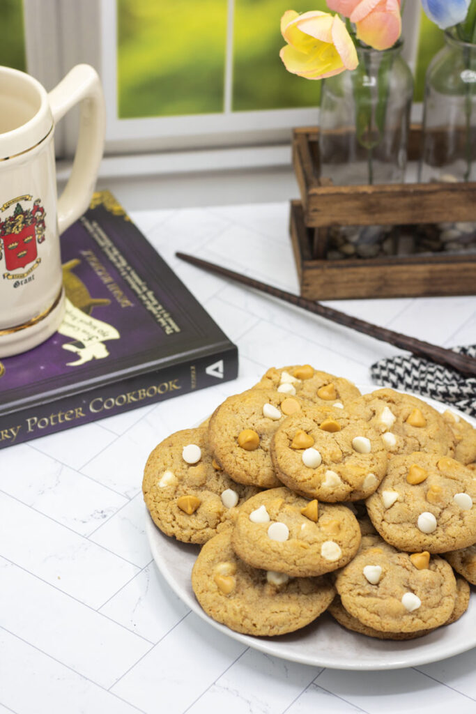 Butterbeer cookies on a plate with a mug, harry potter cookbook, and wand nearby