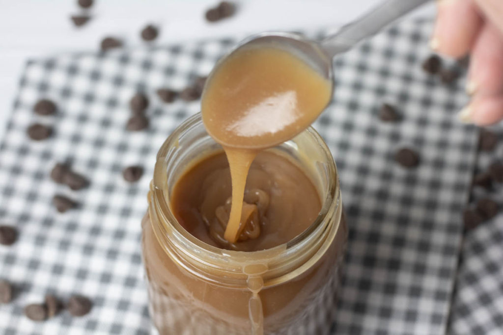 spoon drizzling salted caramel sauce into a mason jar