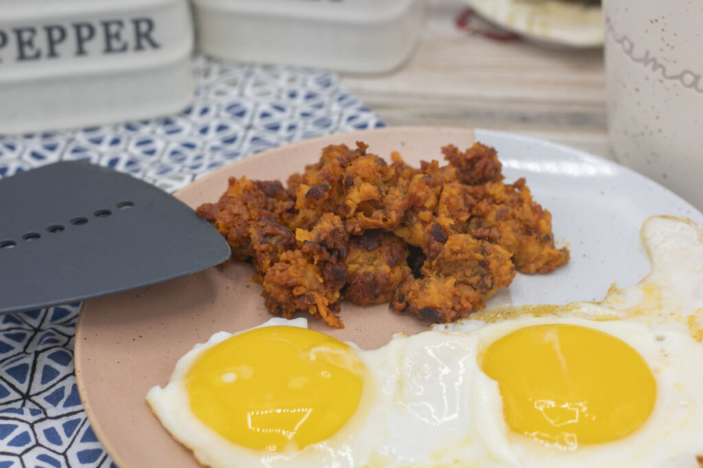 Spatula adding chorizo hash to the plate with eggs