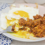 A fork scooping egg yolk and chorizo potato hash