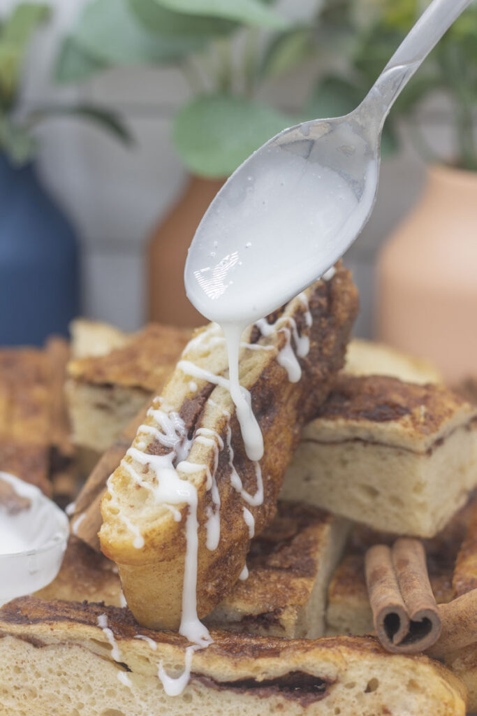 Drizzling spoonfuls of icing on a plate of sweet cinnamon focaccia breadsticks