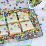 Mini m&ms pouring onto a plate filled with m&ms and cosmic blondies sitting on top