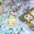 A cosmic blondie on a plate beside a platter of blondies and mini m&ms scattered around