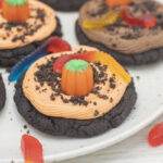 dark chocolate cookies with orange icing and pumpkins and gummy worms