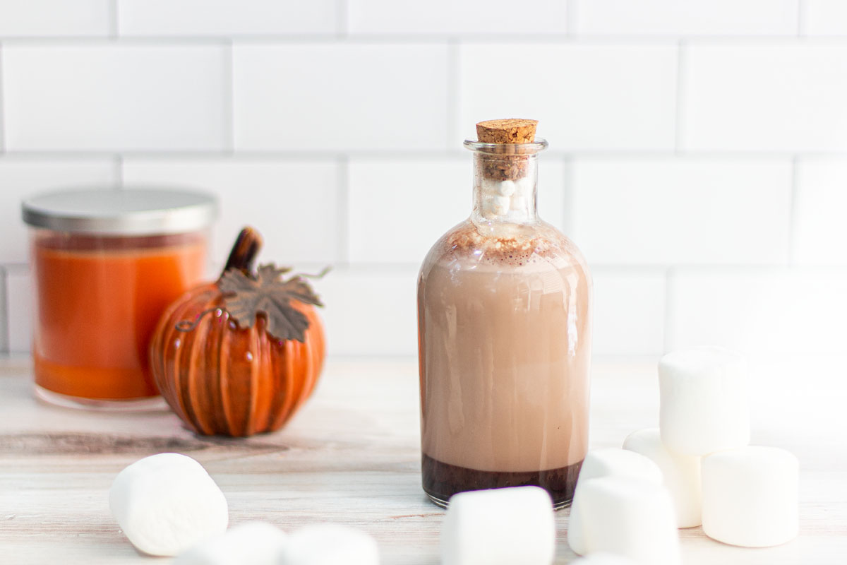 Dragon's milk hot chocolate cocktail in a potion bottle, surrounded by pumpkins, candles, and marshmallows