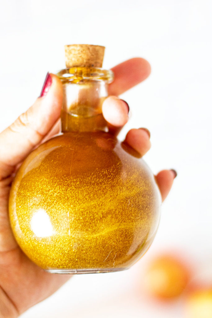 Hand holding a round potion bottle with swirling gold liquid