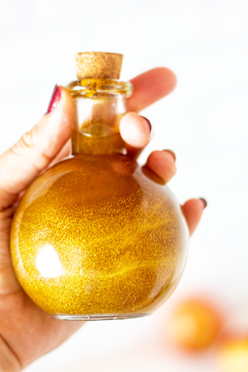 Hand holding a round potion bottle with swirling gold liquid