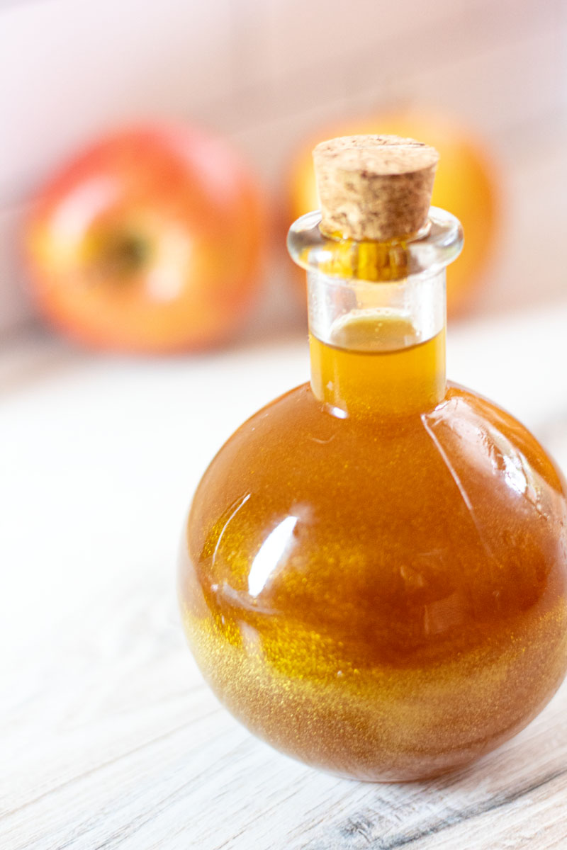 Round potion bottle of swirling gold felix felicis, a Harry Potter inspired Halloween cocktail, and apples in the background