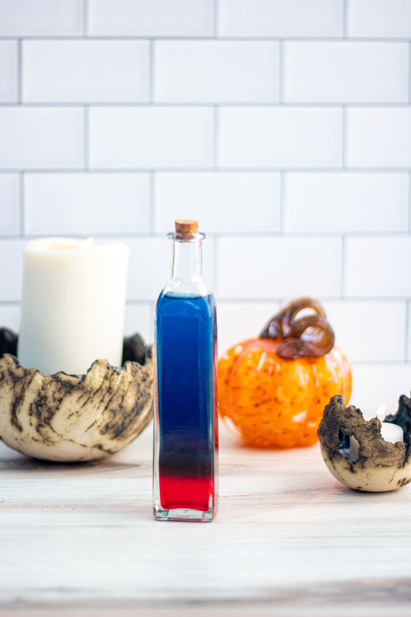Halloween Cocktail in a tall and skinny potion bottle, with blue liquid sitting on red liquid