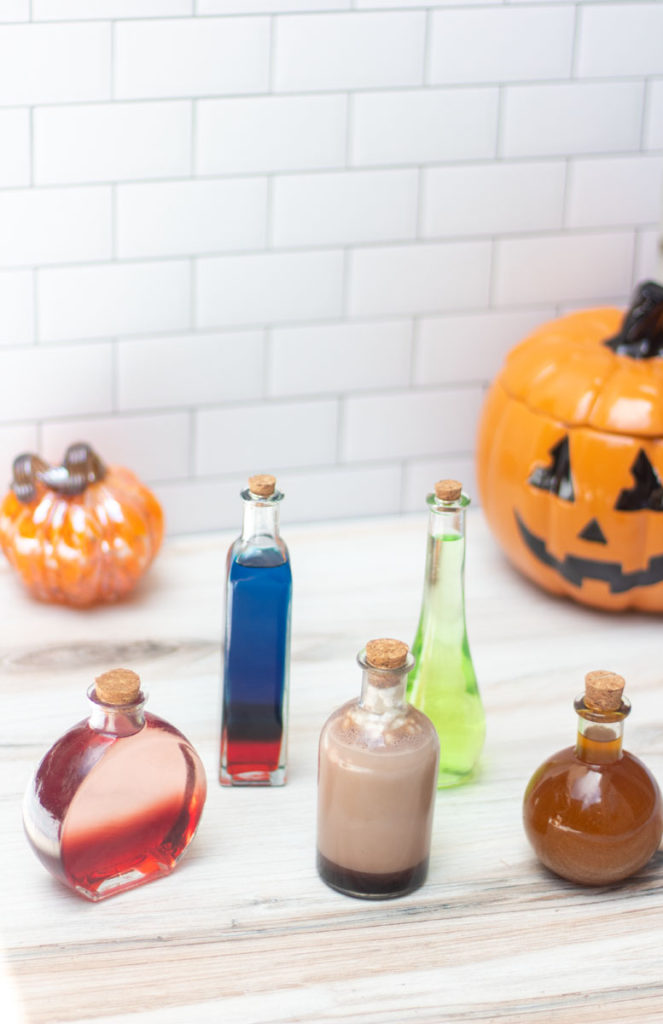 Five potion bottles containing various Halloween cocktails with pumpkins in the background