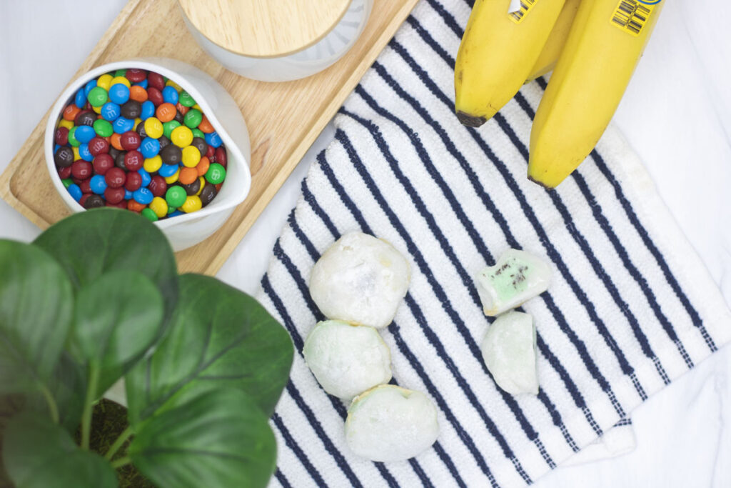 Mint chocolate chip ice cream mochi scattered around bananas and a dish of mini m&ms