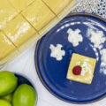 View of key lime pie bars in a tin and a slice on a plate with raspberries and cream
