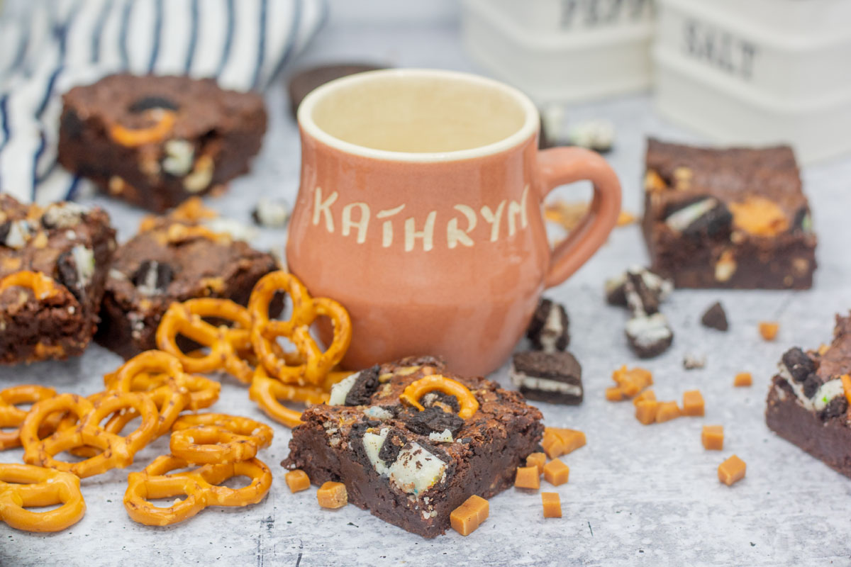 Everything but the kitchen sink brownies tossed with mix-ins around a cup that reads "Kathryn"