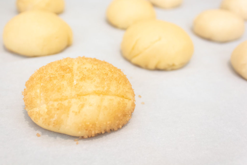 Buns being coated with raw sugar and the crosshatch pattern before the oven