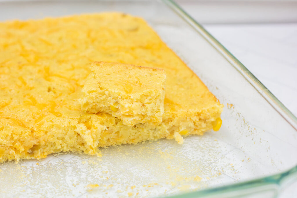 A slice of cornbread atop a pan of cornbread fresh from the oven