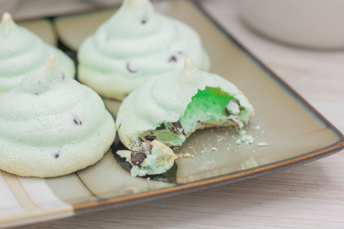 A broken mint chocolate chip meringue on a plate with other meringues