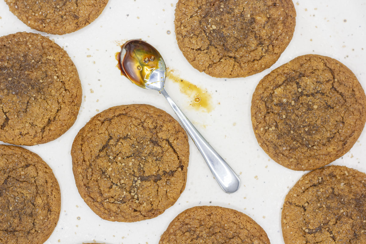 A spoon smeared with molasses surrounded by molasses cookies
