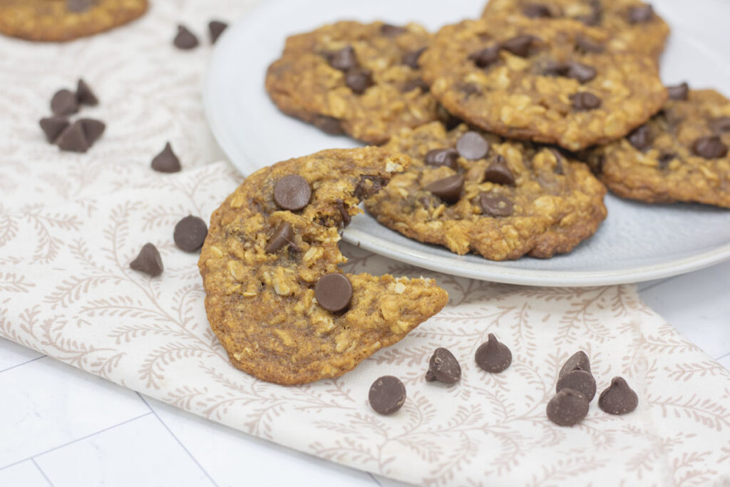 A plate of oatmeal chocolate chip cookies, one with a bite taken out of it leaned against the plate