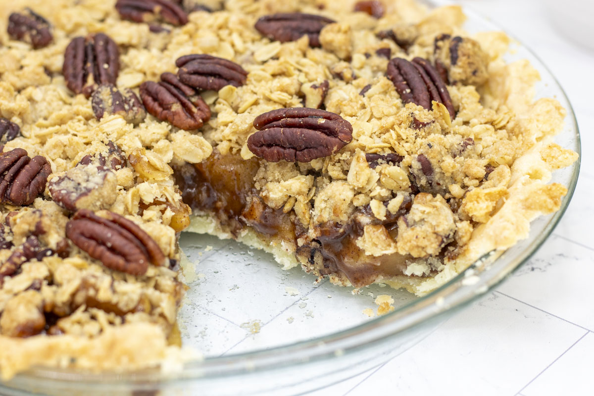 Slice missing from pecan streusel apple pie so you can see the layers of crust, apple filling, and pecan streusel