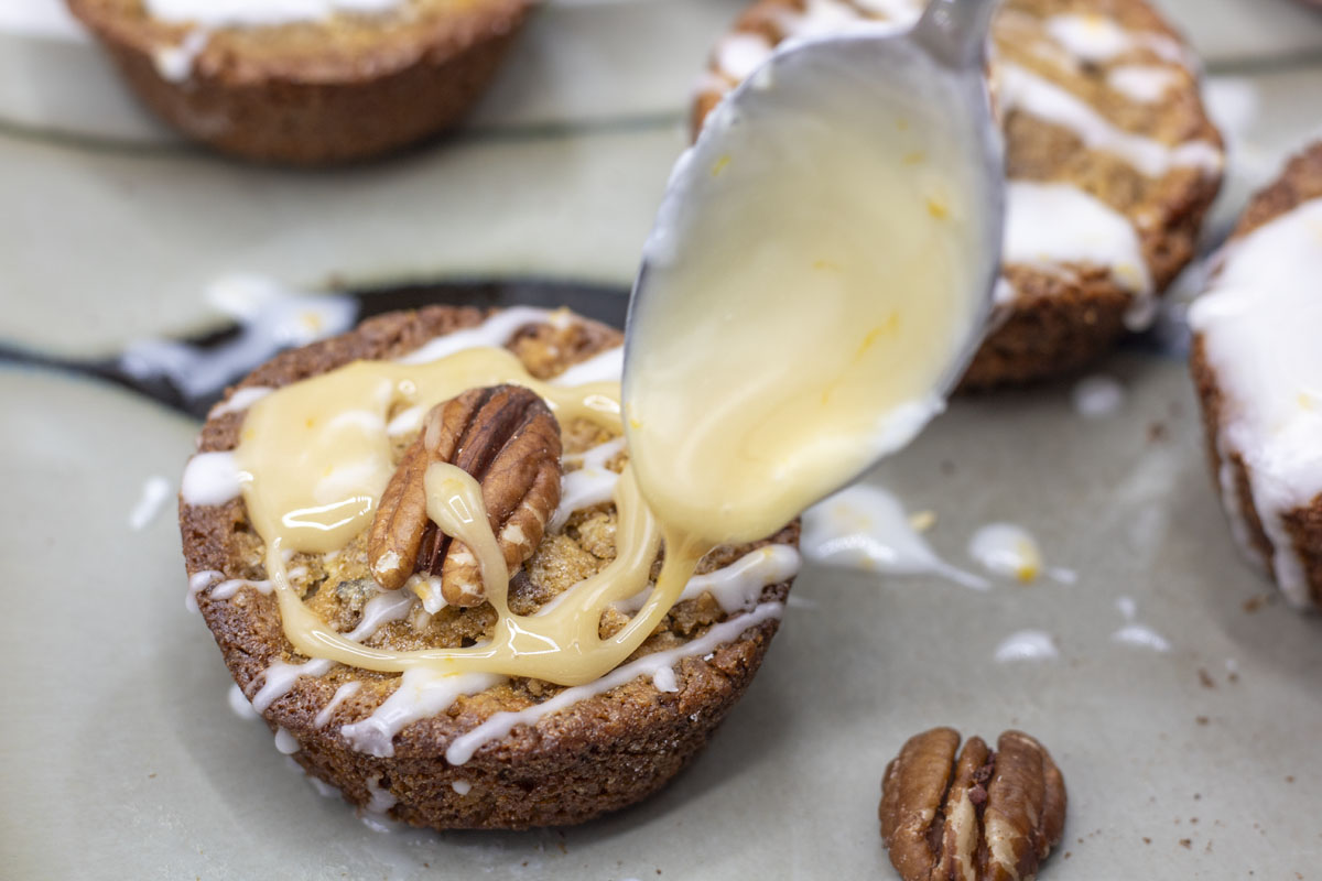 Spoon drizzling maple icing on a muffin