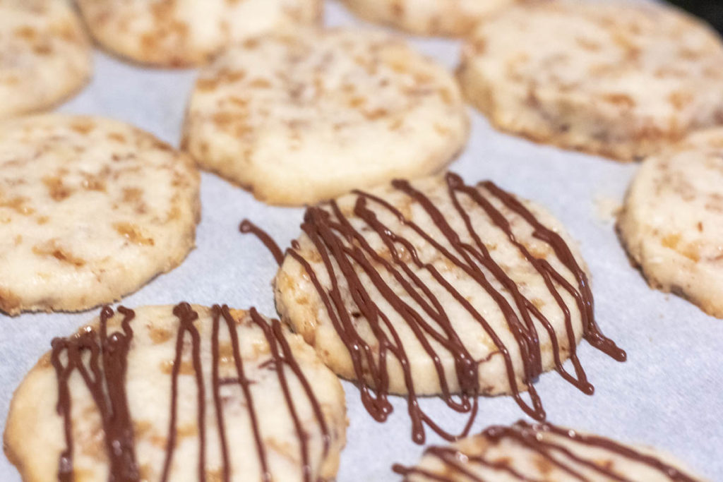 drizzling chocolate over pecan toffee cookies