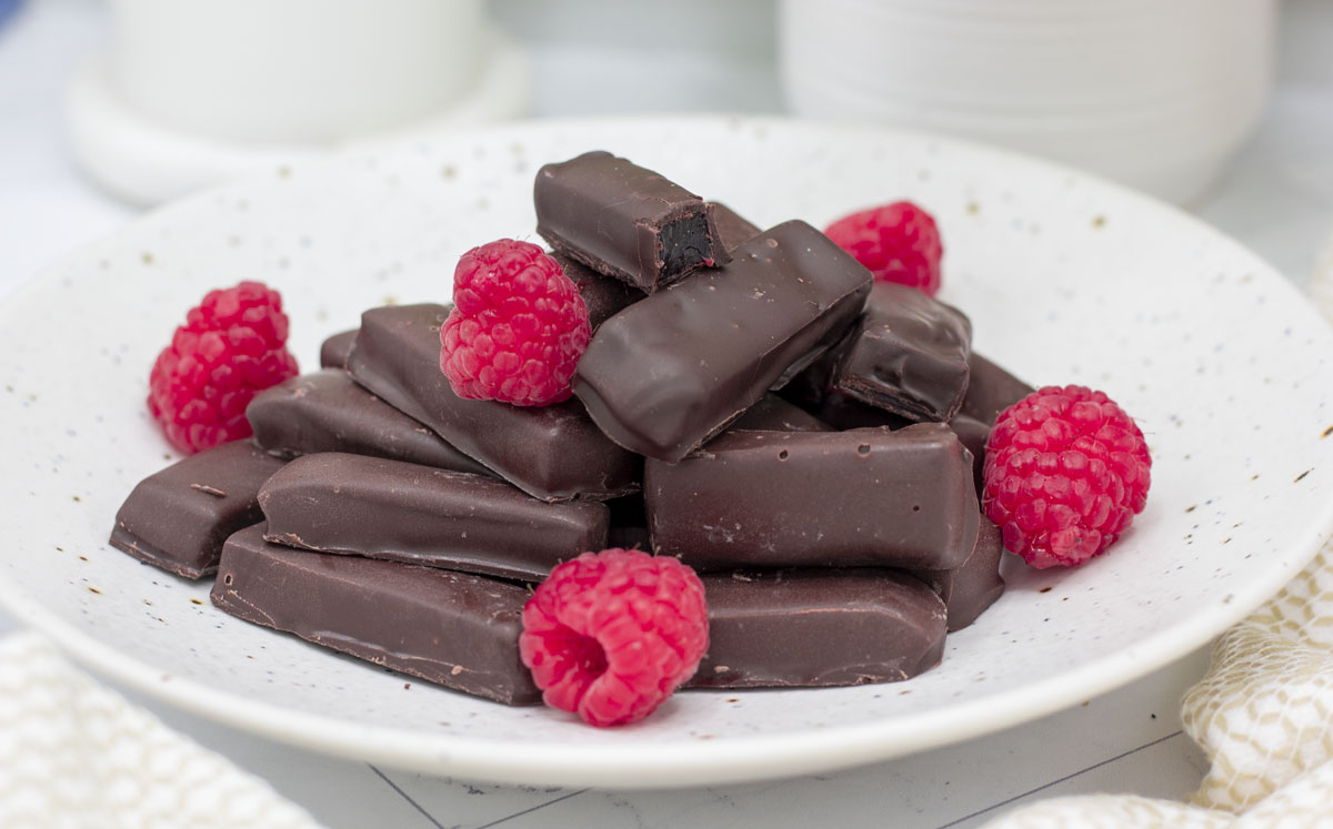 Raspberry jelly "rings" in a stick shape, piled high in a bowl with fresh raspberries