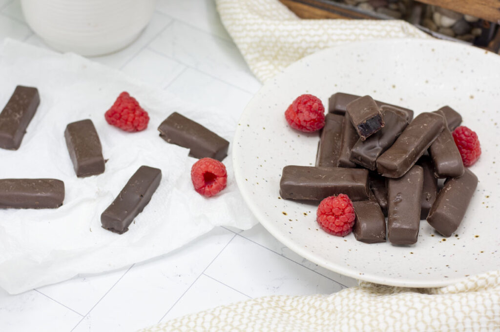 Serving plate of raspberry jelly "rings" in a stick shape with others and raspberries scattered nearby