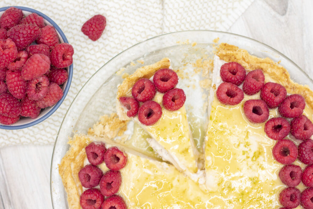 Slice of raspberry lime cheesecake in a pie with raspberries nearby