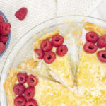 Slice of raspberry lime cheesecake in a pie with raspberries nearby