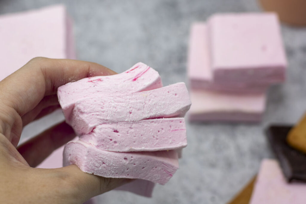 Hand squishing a stack of homemade raspberry marshmallows