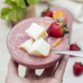 Hand lifting a glass of reverse strawberry shortcake with partially submerged pound cake