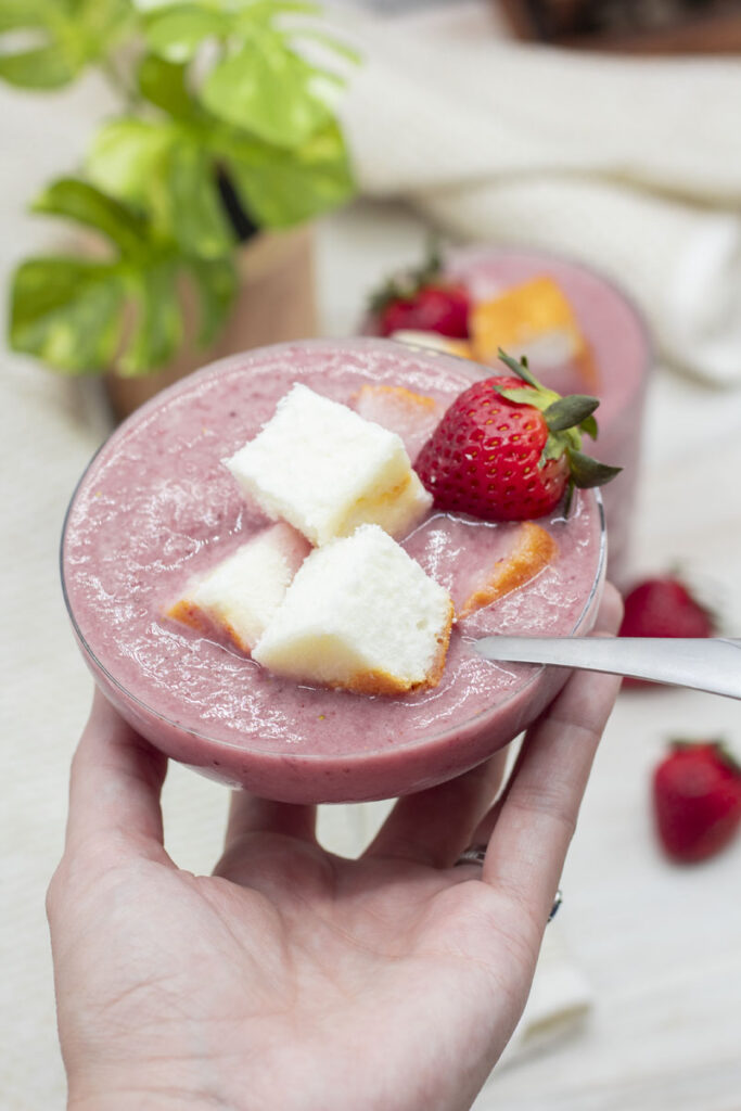 Hand lifting a glass of reverse strawberry shortcake with partially submerged pound cake