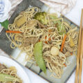 Slow cooker lo mein on a plate surrounded by sauces and flowers