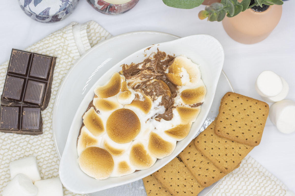 S'mores dip with a bite taken out of it so you can see the swirl of marshmallows and chocolate beneath the marshmallow crust