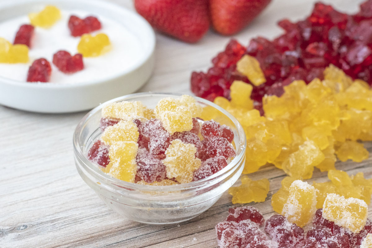 sour gummies in a bowl next to cherry and lemon gummies